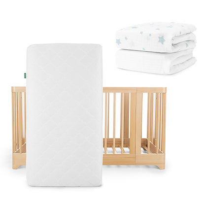 The Newton Baby Nest Convertible Crib with the Original Mattress is shown, with two white fitted crib sheets—including a Breathable Organic Cotton Sheet in a blue star pattern—stacked beside it.