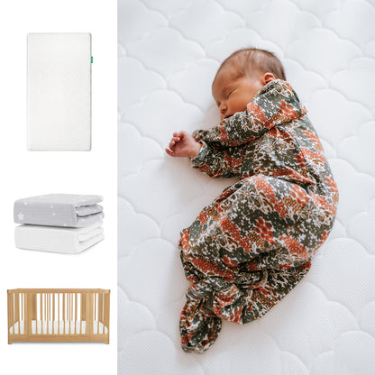 A baby in a floral onesie sleeps on the Newton Baby Nest Convertible Crib, Original Mattress, & Sheets set. To the left are images of the crib, two folded breathable organic cotton sheets, and a wooden crib. 111-8420-NAT-1000-WHT-SGW