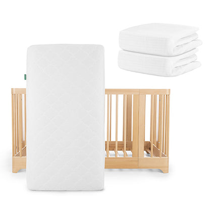 The Newton Baby Nest Convertible Crib features light wood and white bars, paired with the Original Mattress from the Nest Sleep Bundle and two neatly folded white crib sheets.