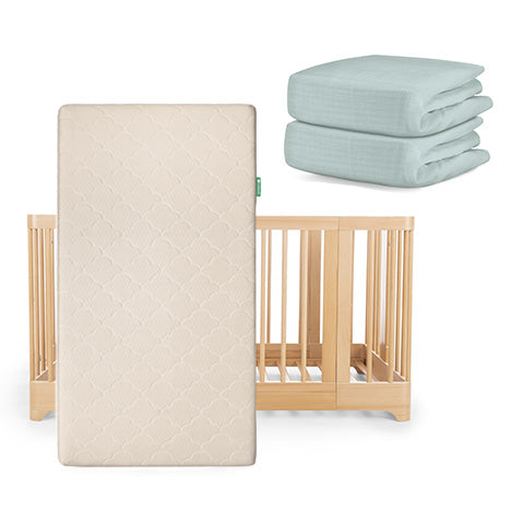 The Newton Baby Nest Convertible Crib, Original Mattress, and two folded light blue crib sheets—including a Breathable Organic Cotton Sheet—are displayed together.