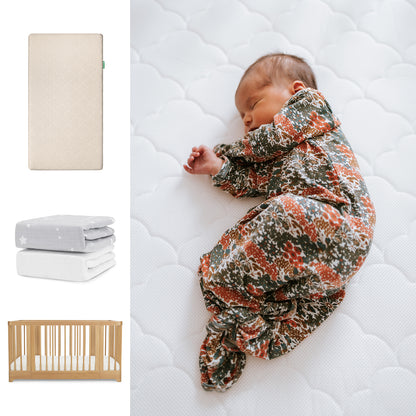 A newborn sleeps on a Newton Baby Nest Convertible Crib with the Original Mattress and sheets; nearby are folded blankets, crib mattress images, and the stylish Newton Baby products. 111-8420-NAT-1000-SAN-SGW