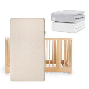The Newton Baby Nest Convertible Crib, Original Mattress, and two sheets—one gray with stars and one breathable organic cotton—are displayed, with the light wood crib and beige mattress standing vertically in front.