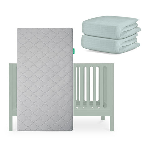 The Newton Baby Galileo Crib in light green is shown with the Original Crib Mattress propped upright in front and two folded light green organic cotton sheets stacked beside it. skip