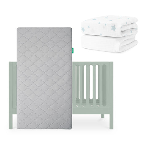 The Newton Baby Galileo Crib (light green) features the Original Crib Mattress (gray), propped vertically in front, with star-patterned sheets and a folded white blanket with blue stars placed nearby. skip