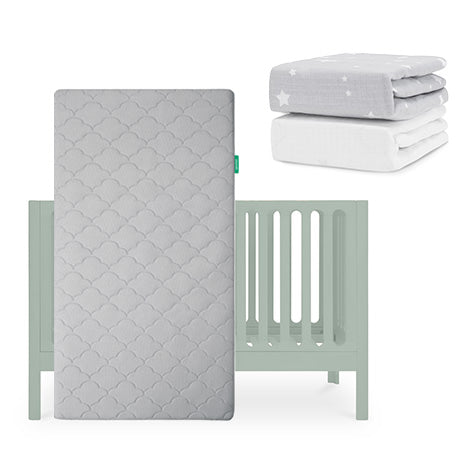 The Newton Baby Galileo Crib is shown with the Original Crib Mattress standing upright. Two sheets—a gray with white stars and a solid organic cotton—are folded nearby. skip