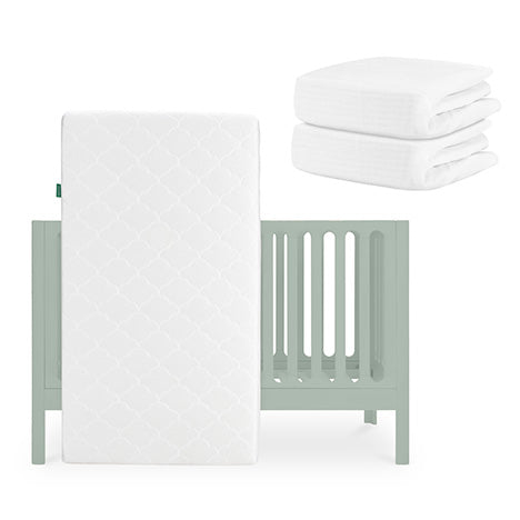The Newton Baby Galileo Crib in light green with the Original Crib Mattress leaning against it, plus two folded breathable organic cotton sheets stacked nearby. skip