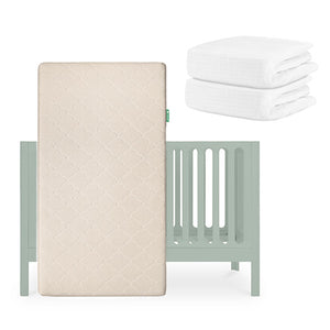 A light green Newton Baby Galileo Crib with the Original Crib Mattress upright in front and two folded white Breathable Organic Cotton Sheets beside it, all against a white background. skip