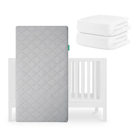 A gray, patterned Newton Baby Original Crib Mattress stands upright in front of the Galileo Crib, with two folded white sheets stacked beside it on a white background. skip