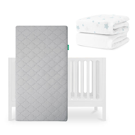 The Newton Baby Galileo Crib, Original Crib Mattress, and Sheets are shown: a gray breathable mattress stands upright by the crib, with two folded sheets—one organic cotton and one white with blue stars—in the top right corner. skip