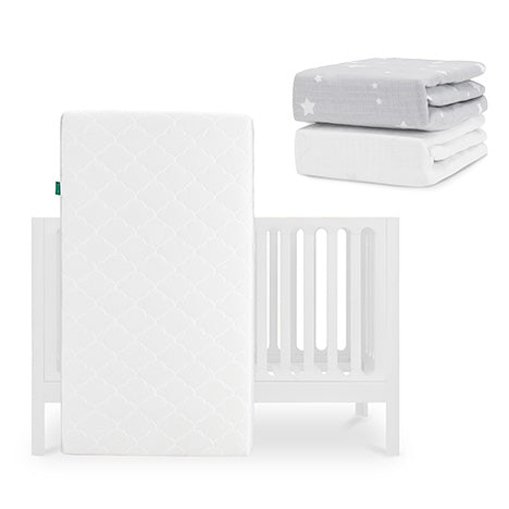 The Newton Baby Galileo Crib with the Original Crib Mattress stands upright, while two folded fitted sheets—a gray star-patterned and a Breathable Organic Cotton Sheet—are stacked nearby. skip