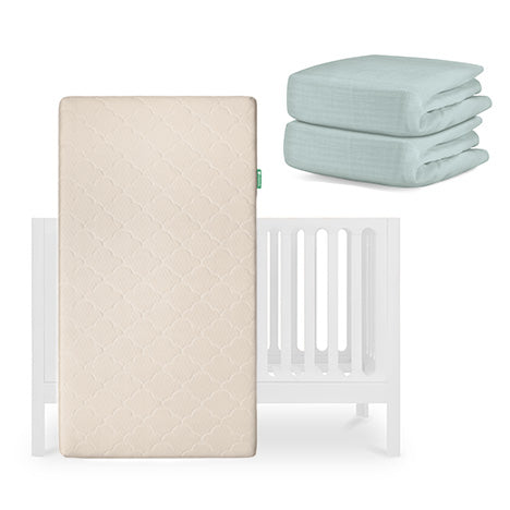 The Newton Baby Galileo Crib is displayed with the Original Crib Mattress standing upright and two folded light green organic cotton sheets stacked neatly beside it. skip