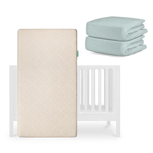 The Newton Baby Galileo Crib is displayed with the Original Crib Mattress standing upright and two folded light green organic cotton sheets stacked neatly beside it. skip