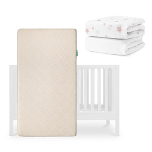 A beige Newton Baby Original Crib Mattress stands upright before a white Galileo Crib, with folded sheets—including a breathable organic cotton sheet with pink stars—shown in the upper right corner. skip