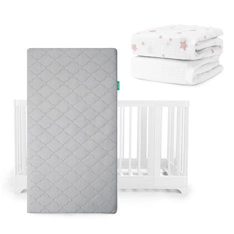 A gray Newton Baby Original Mattress stands upright before a white Nest Convertible Crib, with folded Breathable Organic Cotton Sheets—one with pink stars, one white—stacked above and to the right.