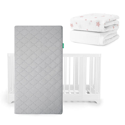 A gray Newton Baby Original Mattress stands upright before a white Nest Convertible Crib, with folded Breathable Organic Cotton Sheets—one with pink stars, one white—stacked above and to the right.