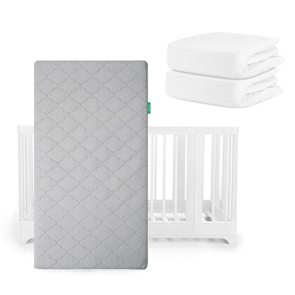A gray scalloped Newton Baby Original Mattress stands before a white Nest Convertible Crib, with two folded white sheets stacked at its upper right.