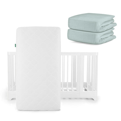 A white Newton Baby Nest Convertible Crib with an Original Mattress stands upright, with two folded light blue breathable organic cotton sheets stacked nearby.