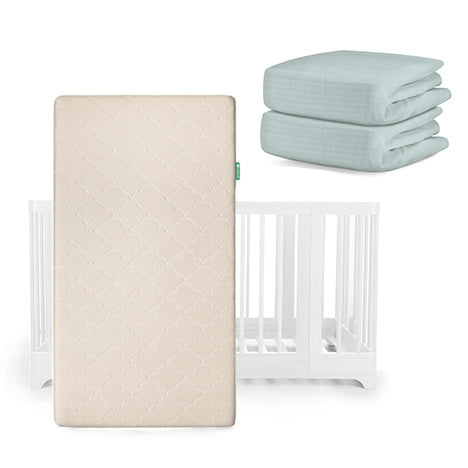 A Nest Convertible Crib by Newton Baby with the Original Mattress in beige in front, plus two folded light blue Breathable Organic Cotton Sheets stacked beside it.