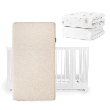 The Newton Baby Nest Convertible Crib, Original Mattress, and Sheets set is shown with a beige breathable mattress standing upright before the white crib, plus two fitted sheets stacked behind—one adorned with pink stars.