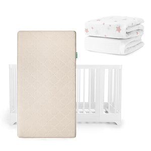 The Newton Baby Nest Convertible Crib, Original Mattress, and Sheets set is shown with a beige breathable mattress standing upright before the white crib, plus two fitted sheets stacked behind—one adorned with pink stars.