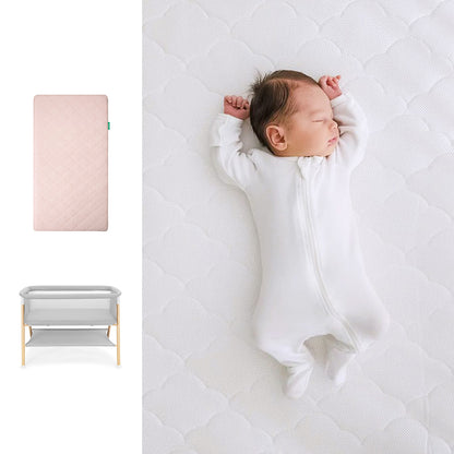 Newborn baby wrapped in a white blanket on a white mattress, with a pink mattress and gray bassinet in the corner. 1000-pnk-8402 