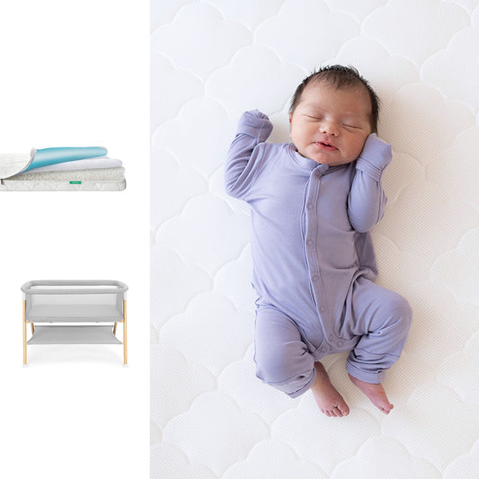 Baby in a purple onesie lying on a white surface with a changing table and mat in the background. 1001-wht-8402