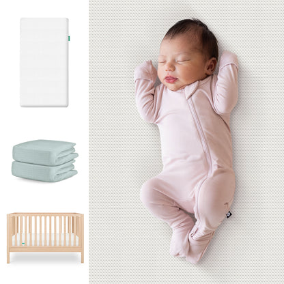 A baby in a light pink sleeper rests on the Newton Baby Essential Crib Mattress. To the left are images of the Galileo Crib, mattress, and folded sheets from the Galileo Crib, Essential Crib Mattress, & Sheets Bundle. 111-8420-NAT-1300-WHT- SNS