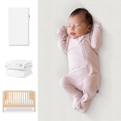 A baby sleeps in a pale pink onesie on the Newton Baby Galileo Crib, Essential Crib Mattress, & Sheets Bundle. To the left are images of the mattress, a star-patterned sheet, and the light wood crib. 111-8420-NAT-1300-WHT-PSW