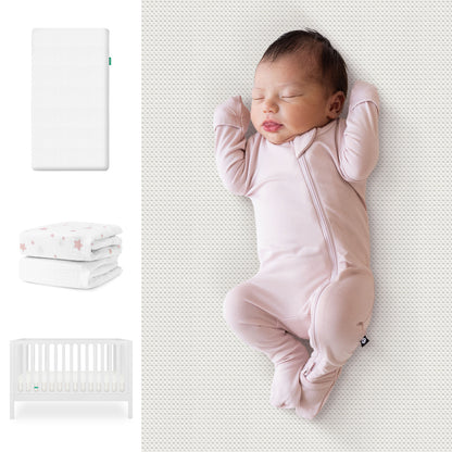 A baby sleeps in a pink onesie on the Newton Baby Galileo Crib, Essential Crib Mattress, & Sheets Bundle. To the left are images of the crib, mattress, and star-patterned bedding from Newton Baby. 111-8420-WHT-1300-WHT-PSW