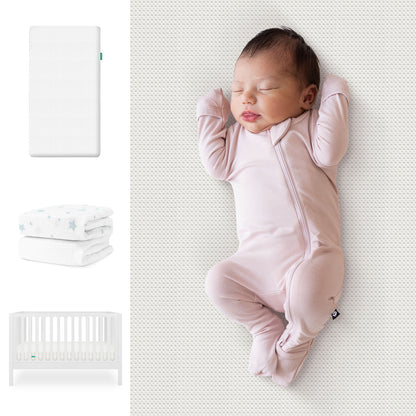 A baby sleeps on a white mattress in a pink onesie. Nearby are the Newton Baby Galileo Crib, Essential Crib Mattress, and Sheets Bundle. 111-8420-WHT-1300-WHT-SDW