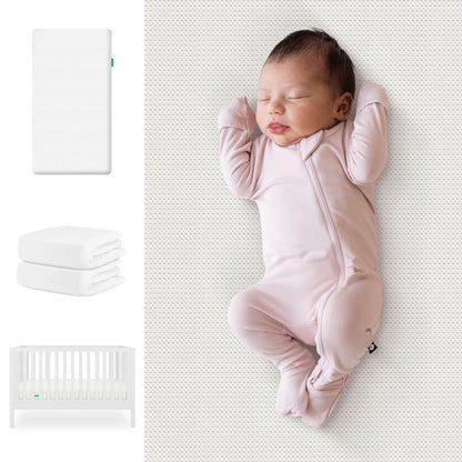 A baby sleeps in a pink onesie on a patterned mattress. To the left are Newton Baby's Galileo Crib, Essential Crib Mattress, and Sheets Bundle. The crib is white with vertical slats; the set also includes folded white sheets. 111-8420-WHT-1300-WHT-WNW