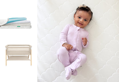 A smiling baby wearing a light purple onesie lies on a white mattress. To the left, a close-up highlights Newton Baby’s Essential Bassinet + Waterproof Mattress with its blue layer and wooden frame design.