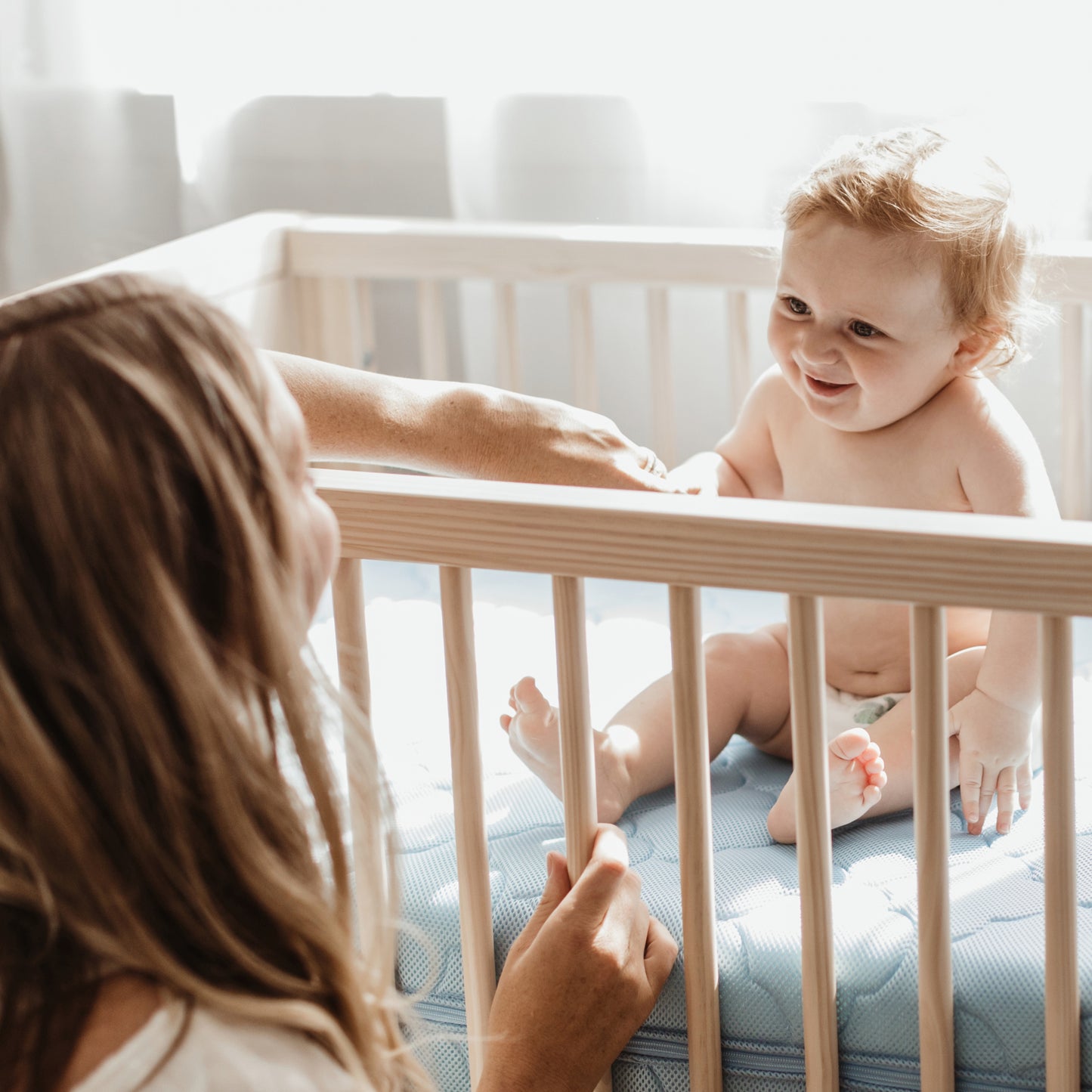 cute baby sitting on newton crib mattress looking at its mother