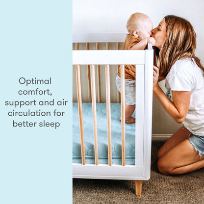 mother holding baby and kissing it while baby stands on blue newton mattress with text "optimal comfort support and air circulation for better sleep"
