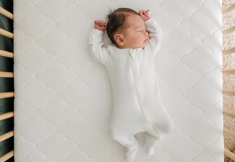 Newborn sleeping peacefully on a Newton Baby breathable crib mattress.