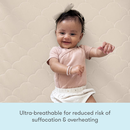 A happy baby in pink lies on a Newton Baby Crib Mattress, known for its ultra-breathable, washable design that reduces risks of suffocation and overheating.