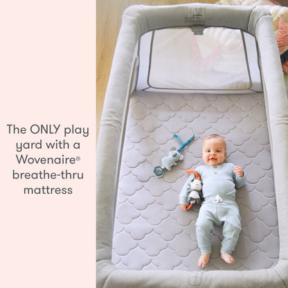baby lying on floor mattress with toys in newton travel crib and play yard with text "the ONLY play yard with a Wovenaire breathe-thru mattress"