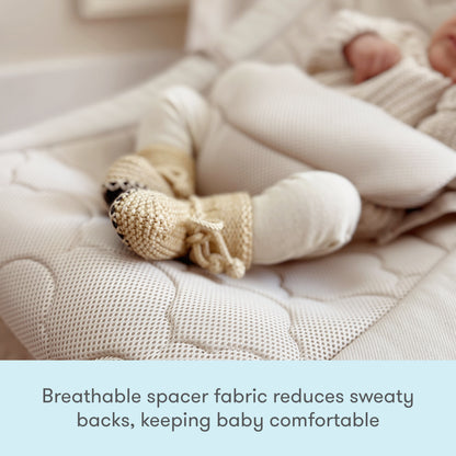 A baby in knit booties and light clothing rests on the Newton Baby Rocker’s soft, breathable quilted mattress with adjustable harness. Text reads: Breathable spacer fabric reduces sweaty backs, keeping baby comfortable.