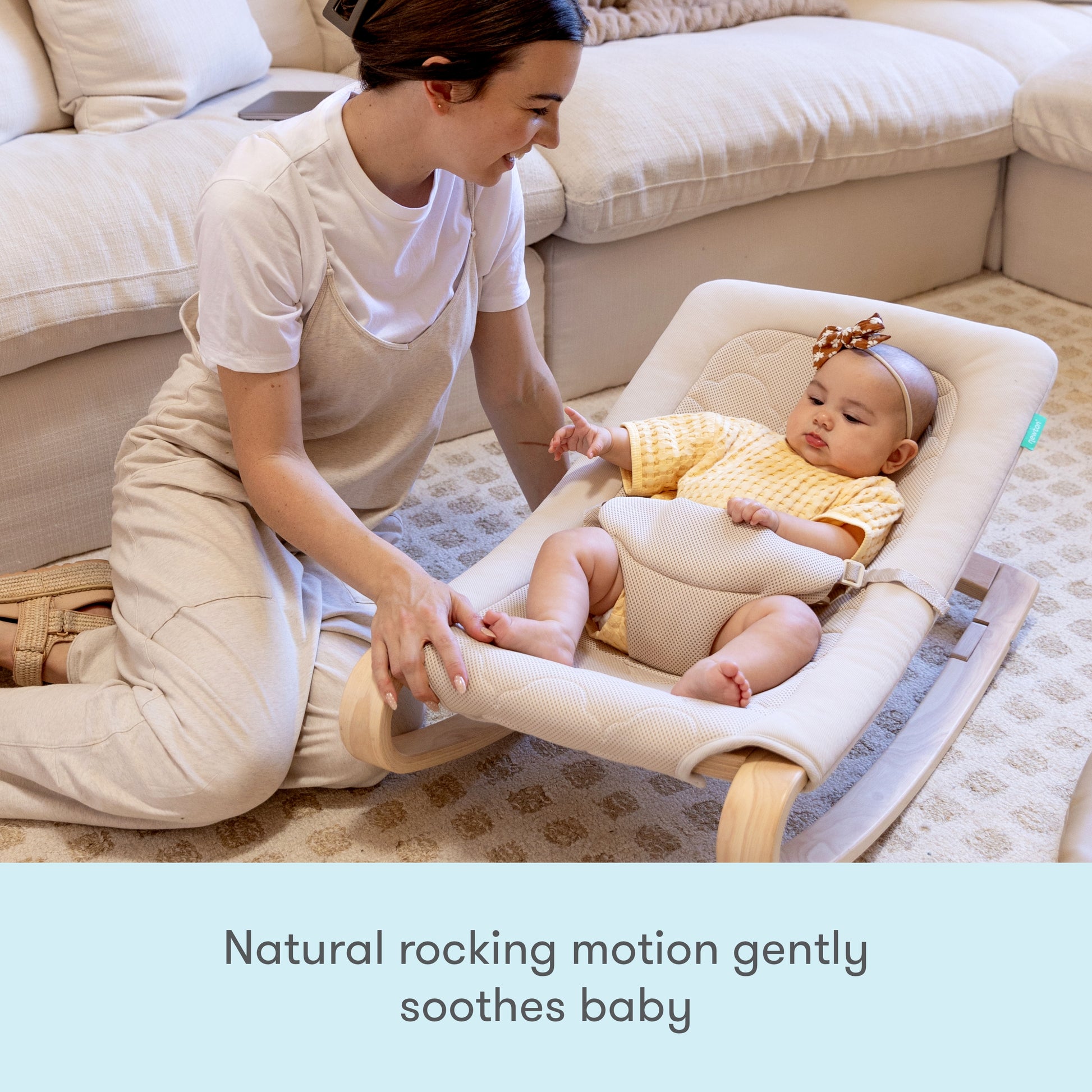 A woman kneels beside a smiling baby in a Newton Baby Rocker. Text below reads, Natural rocking motion gently soothes baby while an adjustable harness keeps your little one secure and comfortable.