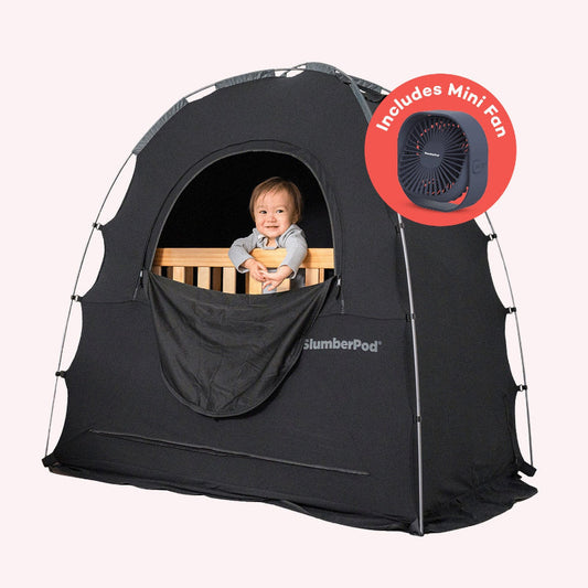 baby sitting in crib, underneath black slumberpod blackout tent, with fan icon