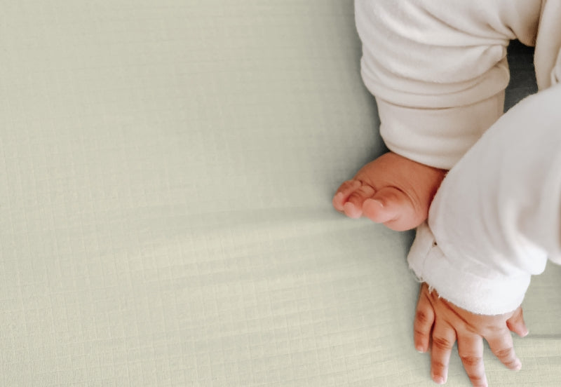 Close-up view of a baby's bare feet and hands on a oatmeal colored blanket, highlighting soft and peaceful tones. 999-3020-ONO 999-3520-ONO