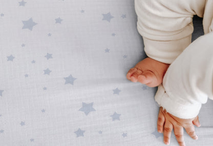 A baby's hand and feet on a soft sheet with a subtle star pattern. 999-3020-SDW 999-3520-SDW