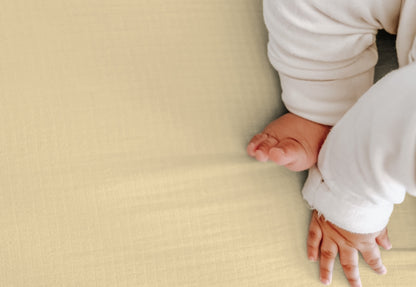 Close-up of a baby's hands resting on a sunshine yellow sheet, clad in a white onesie. 