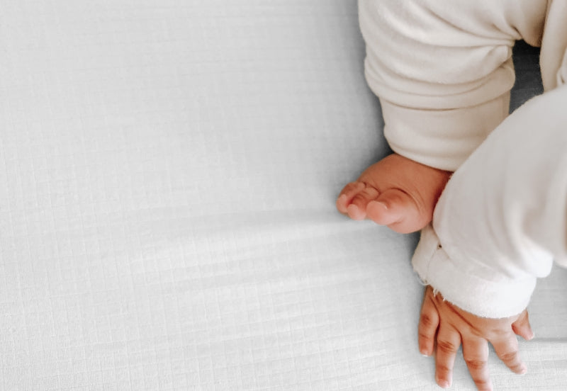 Close-up of a baby’s hand and foot on a textured white sheet. 999-3020-WNW 999-3520-WNW