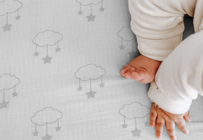 Close-up of a baby's hands and bare feet on a soft sheet with a gentle cloud and star pattern, embodying comfort and serenity. 999-3020-WSW 999-3520-WSW