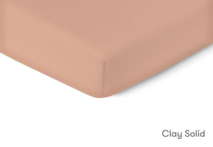 Close-up of a clay solid colored crib mattress sheet with a smooth finish, labelled "Clay Solid." 999-3020-CLY 999-3520-CLY