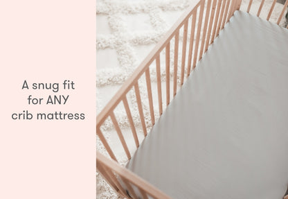Wooden crib with a snugly fitted gray mattress and the text "A snug fit for ANY crib mattress." all