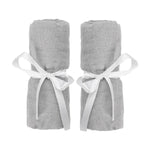 Two rolled-up Newton Baby Compact Travel Crib Sheets in light gray cotton muslin, each tied with a white ribbon bow, are placed side by side against a white background.