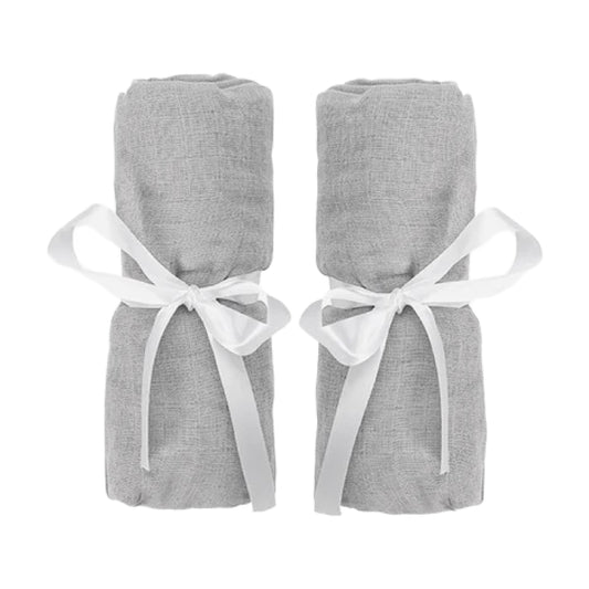 Two rolled-up Newton Baby Compact Travel Crib Sheets in light gray cotton muslin, each tied with a white ribbon bow, are placed side by side against a white background.