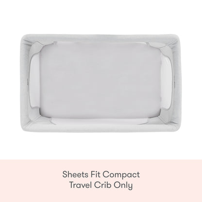 Top-down view of Newton Baby Compact Travel Crib Sheets in white cotton muslin on a light gray crib, with text above that reads, "Sheets Fit Compact Travel Crib Only" on a peach background.